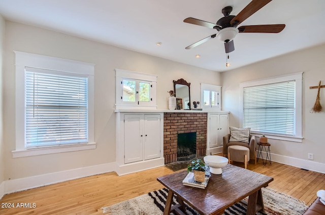 living room featuring a fireplace, light wood-style floors, a ceiling fan, and baseboards
