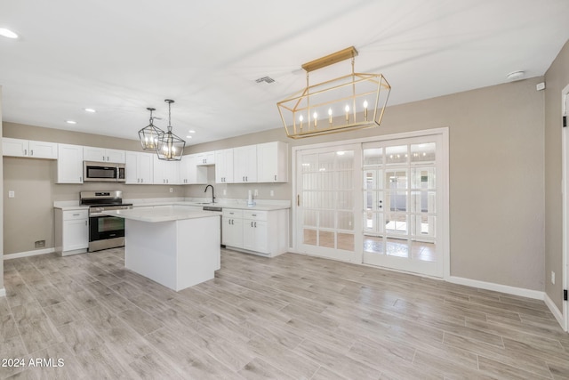 kitchen with stainless steel appliances, hanging light fixtures, a kitchen island, white cabinetry, and light hardwood / wood-style flooring