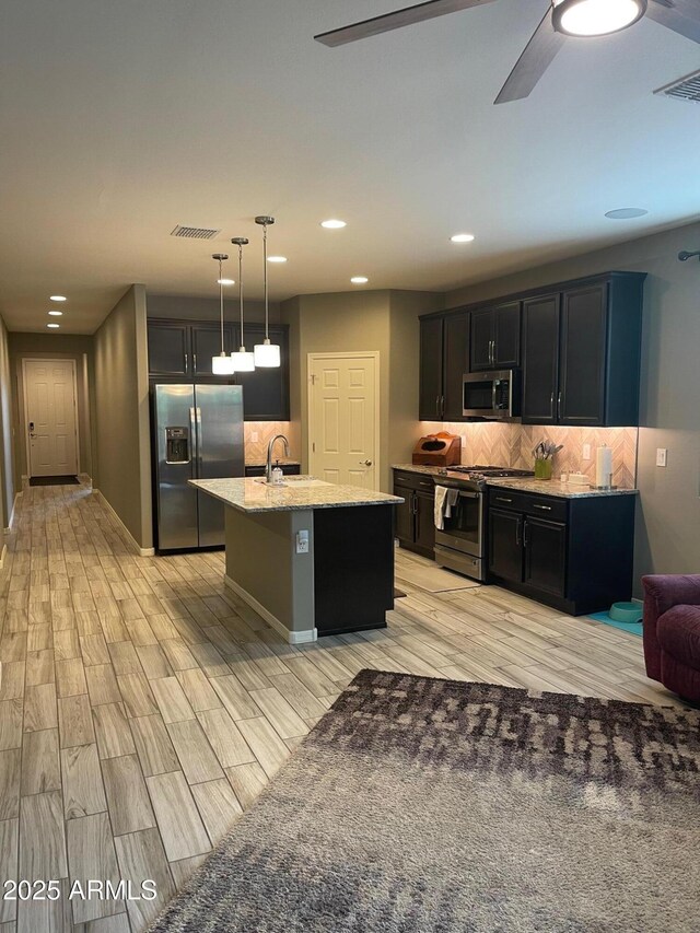 3211 W Pollack St, Phoenix, AZ 85041 - kitchen with stainless steel appliances, backsplash, light wood finished floors, an island with sink, and a ceiling fan