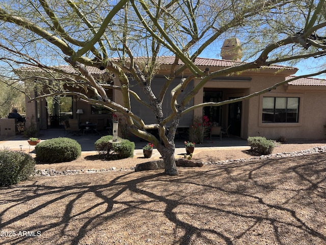 rear view of house featuring stucco siding, a tile roof, a chimney, and a patio area