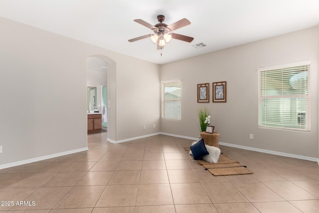 unfurnished room with visible vents, a ceiling fan, arched walkways, light tile patterned floors, and baseboards