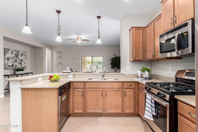 kitchen featuring light stone countertops, a peninsula, a sink, stainless steel appliances, and decorative light fixtures