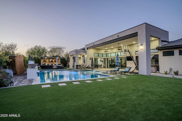 pool at dusk with a lawn, ceiling fan, and a patio area