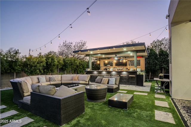 patio terrace at dusk featuring an outdoor hangout area, an outdoor bar, and a lawn