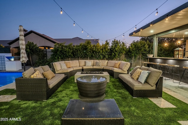 patio terrace at dusk featuring outdoor lounge area, an outdoor bar, and a lawn