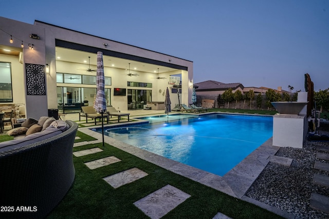 pool at dusk with ceiling fan, an outdoor living space, and a patio area