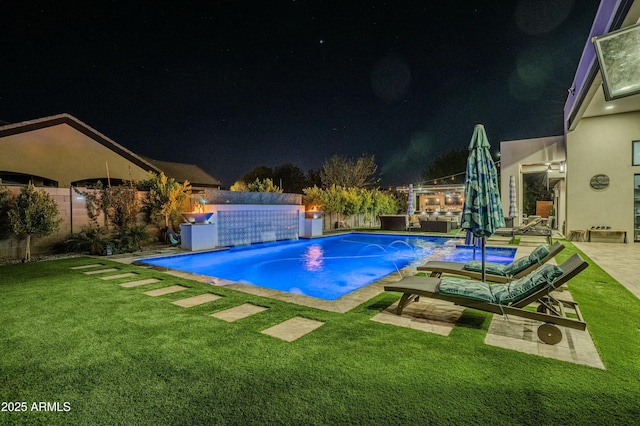 pool at twilight with pool water feature, a yard, and a patio area