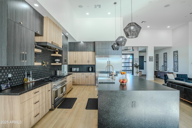 kitchen featuring sink, light hardwood / wood-style flooring, a center island with sink, premium appliances, and pendant lighting