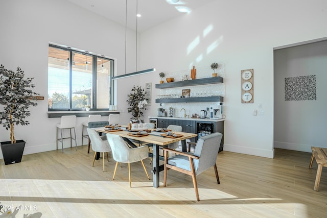 dining area with wet bar, a high ceiling, and light wood-type flooring