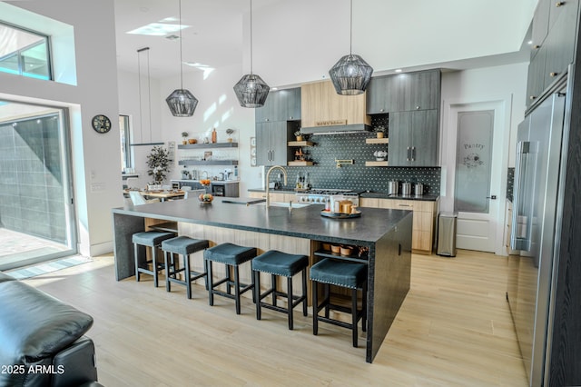 kitchen featuring decorative light fixtures, a kitchen breakfast bar, a kitchen island with sink, light hardwood / wood-style floors, and decorative backsplash