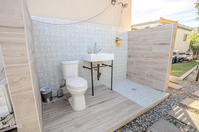 bathroom with walk in shower, toilet, sink, and tile walls