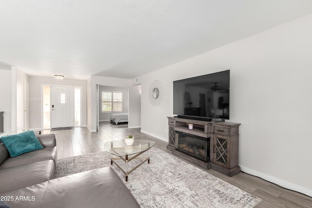 living area with a glass covered fireplace, visible vents, baseboards, and wood finished floors