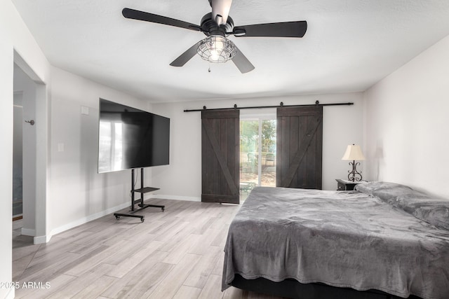 bedroom with baseboards, ceiling fan, a barn door, and light wood-style floors