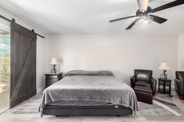 bedroom with ceiling fan, a barn door, and baseboards