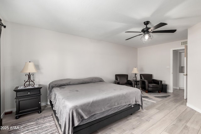 bedroom featuring ceiling fan, a barn door, light wood-style flooring, visible vents, and baseboards