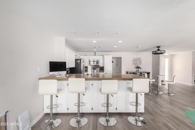 kitchen featuring a breakfast bar area, appliances with stainless steel finishes, white cabinetry, wood finished floors, and a peninsula