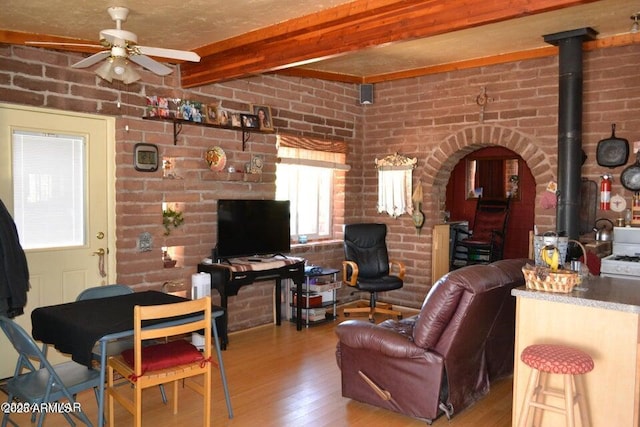 3733 Del Contento Rd, Snowflake, AZ 85937 - living room with wood finished floors, a ceiling fan, beamed ceiling, a wood stove, and brick wall