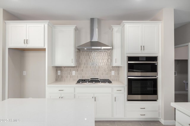 17032 W Cavedale Dr, Surprise, AZ 85387 - kitchen with wall chimney range hood, stainless steel double oven, cooktop, backsplash, and white cabinetry