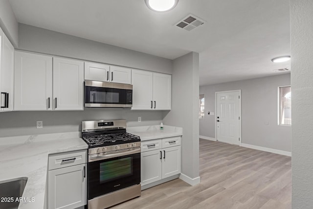 kitchen with light stone counters, light hardwood / wood-style floors, white cabinets, and appliances with stainless steel finishes