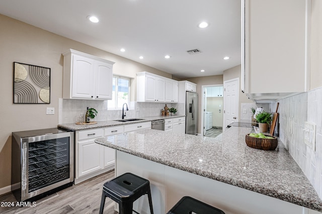 kitchen featuring kitchen peninsula, light hardwood / wood-style flooring, white cabinetry, stainless steel appliances, and beverage cooler