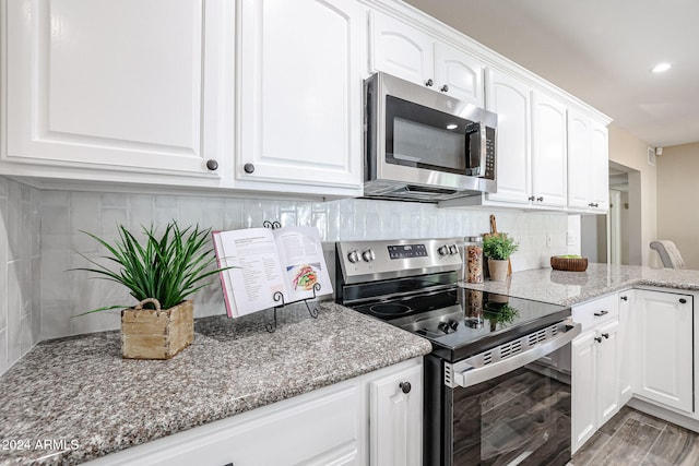 kitchen with white cabinetry, light stone countertops, backsplash, hardwood / wood-style floors, and appliances with stainless steel finishes