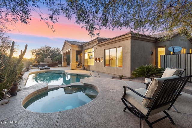 pool at dusk with outdoor lounge area, a patio, and an in ground hot tub