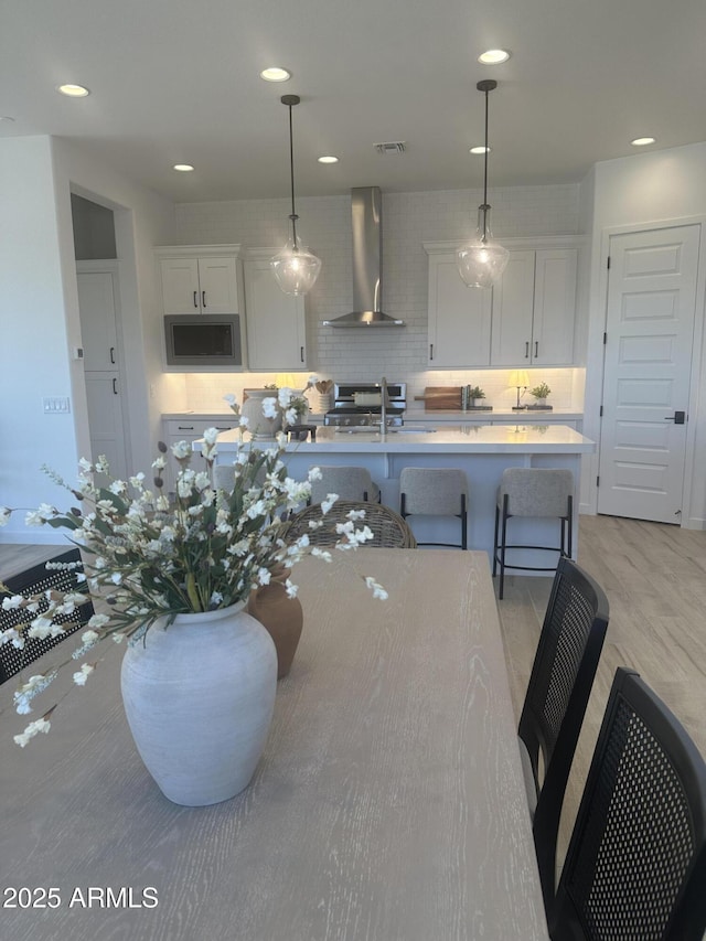 kitchen featuring light countertops, stainless steel microwave, white cabinetry, a sink, and wall chimney range hood
