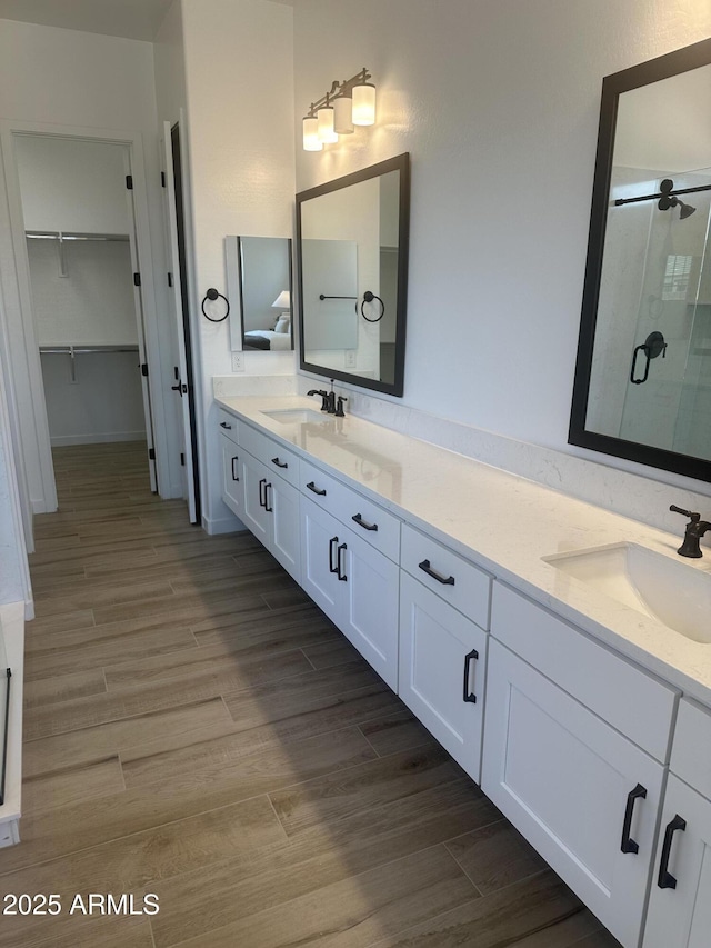 bathroom with double vanity, a sink, a shower stall, and wood finished floors