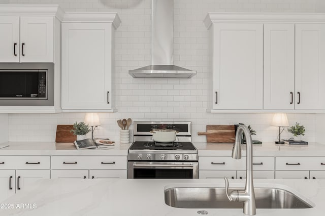 kitchen featuring white cabinetry, stainless steel appliances, backsplash, a sink, and wall chimney exhaust hood