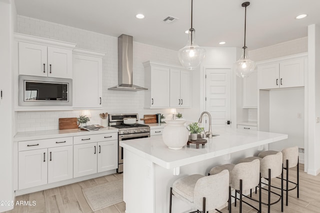 kitchen featuring visible vents, white cabinetry, wall chimney range hood, and stainless steel appliances