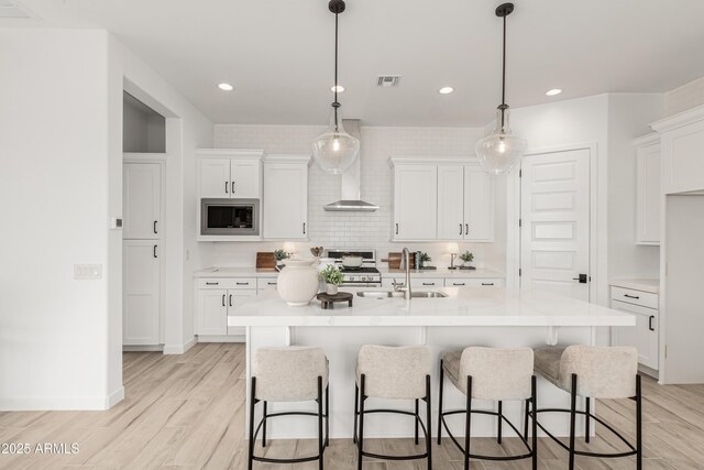 kitchen featuring white cabinets, light countertops, light wood finished floors, a sink, and built in microwave