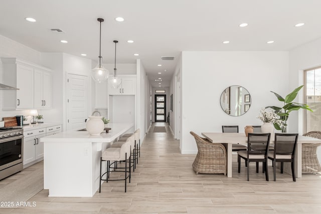 kitchen featuring light countertops, stainless steel gas stove, white cabinetry, a center island with sink, and visible vents