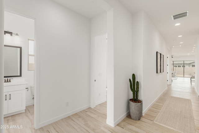 hallway featuring a sink, light wood-style flooring, baseboards, visible vents, and recessed lighting