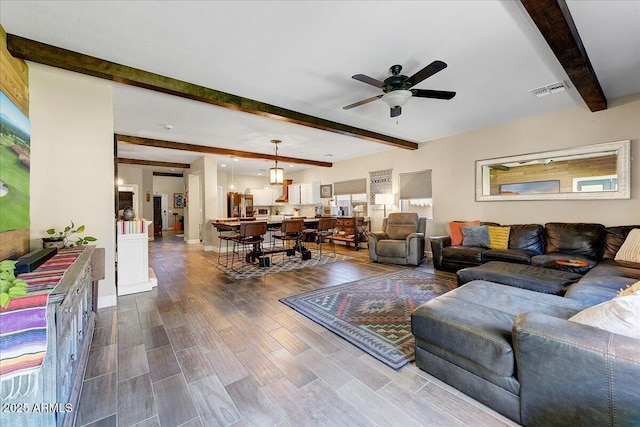 living area with a ceiling fan, beamed ceiling, visible vents, and dark wood-style floors