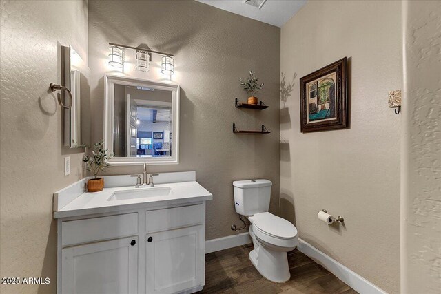 bathroom with toilet, baseboards, wood finished floors, and vanity