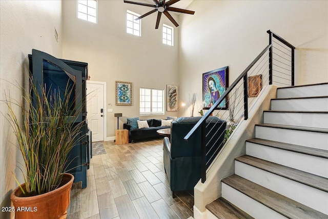 living room with stairs, a ceiling fan, plenty of natural light, and a towering ceiling