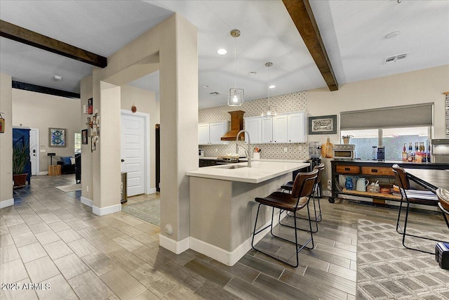 kitchen featuring visible vents, decorative backsplash, a breakfast bar, beamed ceiling, and light countertops