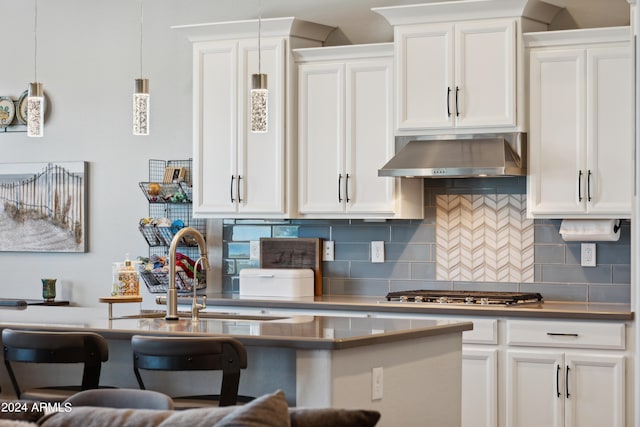 kitchen featuring tasteful backsplash, stainless steel gas cooktop, white cabinetry, hanging light fixtures, and wall chimney range hood