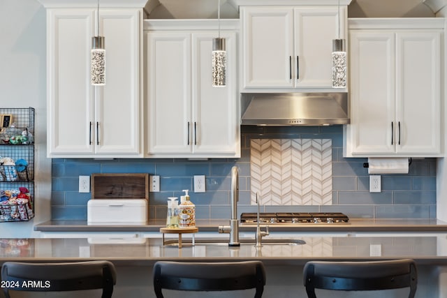 kitchen with backsplash, wall chimney exhaust hood, hanging light fixtures, white cabinets, and stainless steel gas cooktop