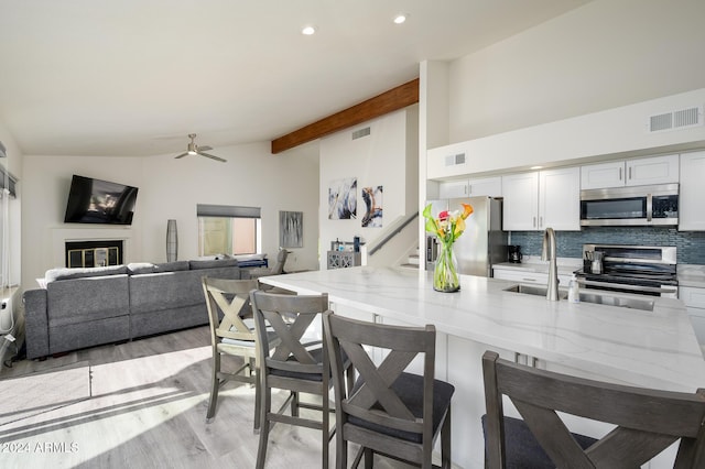 kitchen with a breakfast bar, light hardwood / wood-style flooring, vaulted ceiling with beams, decorative backsplash, and stainless steel appliances