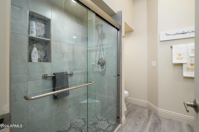 bathroom featuring wood-type flooring, toilet, and a shower with shower door