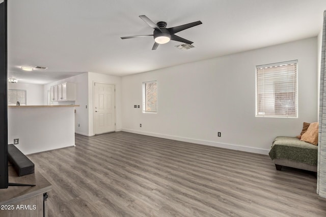 unfurnished living room with ceiling fan, visible vents, baseboards, and wood finished floors