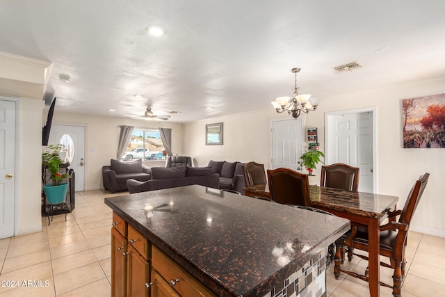 kitchen with a kitchen island, ceiling fan with notable chandelier, hanging light fixtures, dark stone counters, and light tile patterned floors