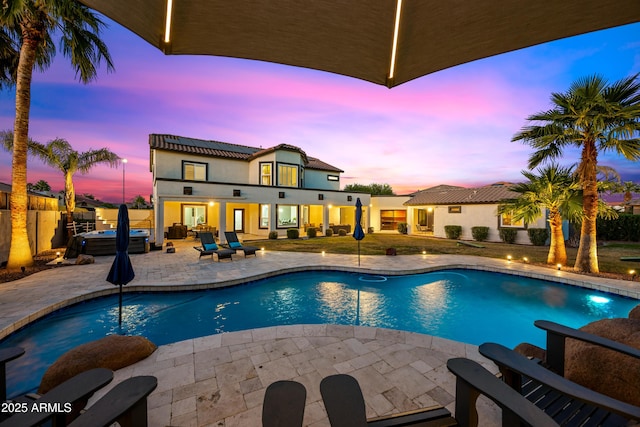 pool at dusk featuring a patio and a hot tub