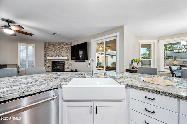 kitchen featuring light stone countertops, dishwasher, sink, a stone fireplace, and white cabinets