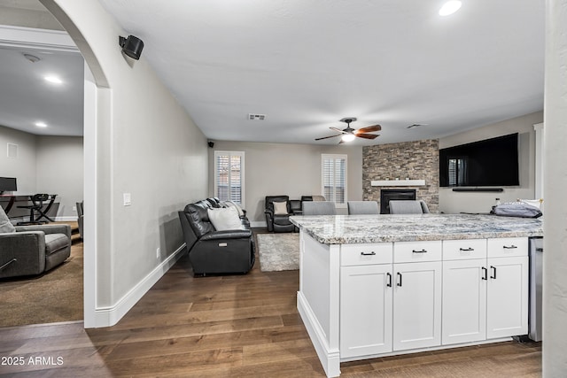 kitchen featuring light stone countertops, ceiling fan, a stone fireplace, dark hardwood / wood-style floors, and white cabinets