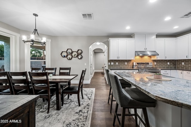 kitchen with white cabinetry, a notable chandelier, pendant lighting, a kitchen bar, and stainless steel stove