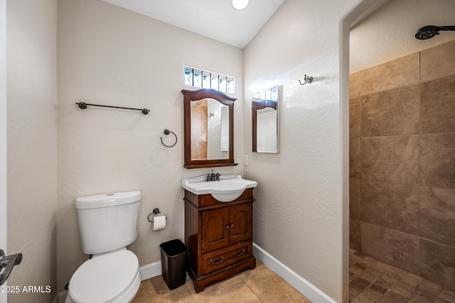 bathroom featuring tile patterned flooring, a tile shower, vanity, and toilet