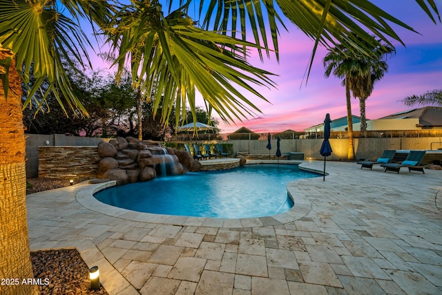 pool at dusk featuring pool water feature and a patio