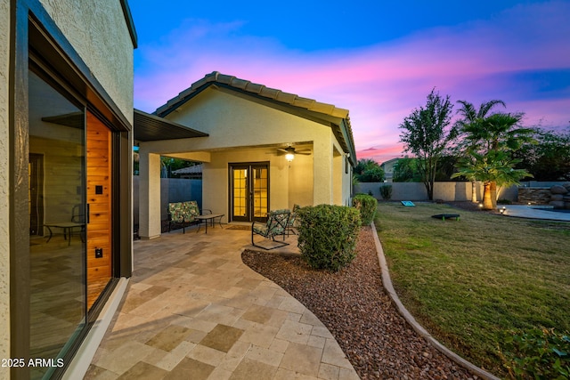 patio terrace at dusk featuring a lawn, ceiling fan, and french doors